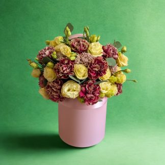 Antique Garden hat box floral arrangement with dusty mauve carnations, soft yellow spray roses in full bloom and bud, and waxflower in a blush pink satin-banded box with silver dollar eucalyptus
